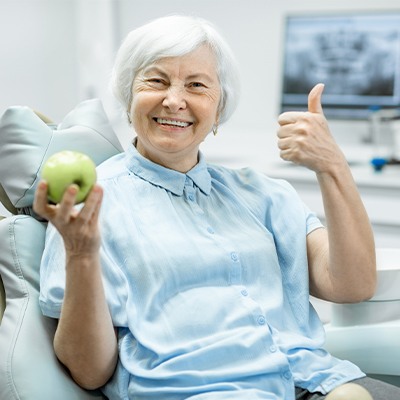 Woman smiling and eating an apple enjoying the benefits of dentures