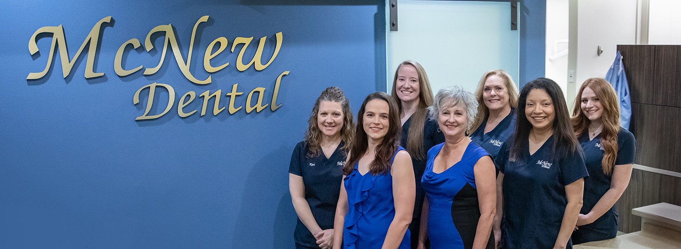 Rockwall Texas dentists and dental team members next to McNew Dental sign on blue wall