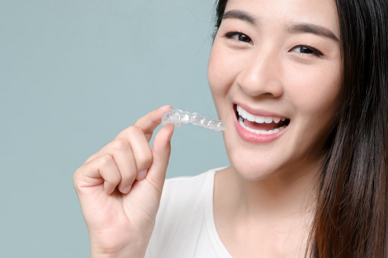 person holding Invisalign aligner and smiling